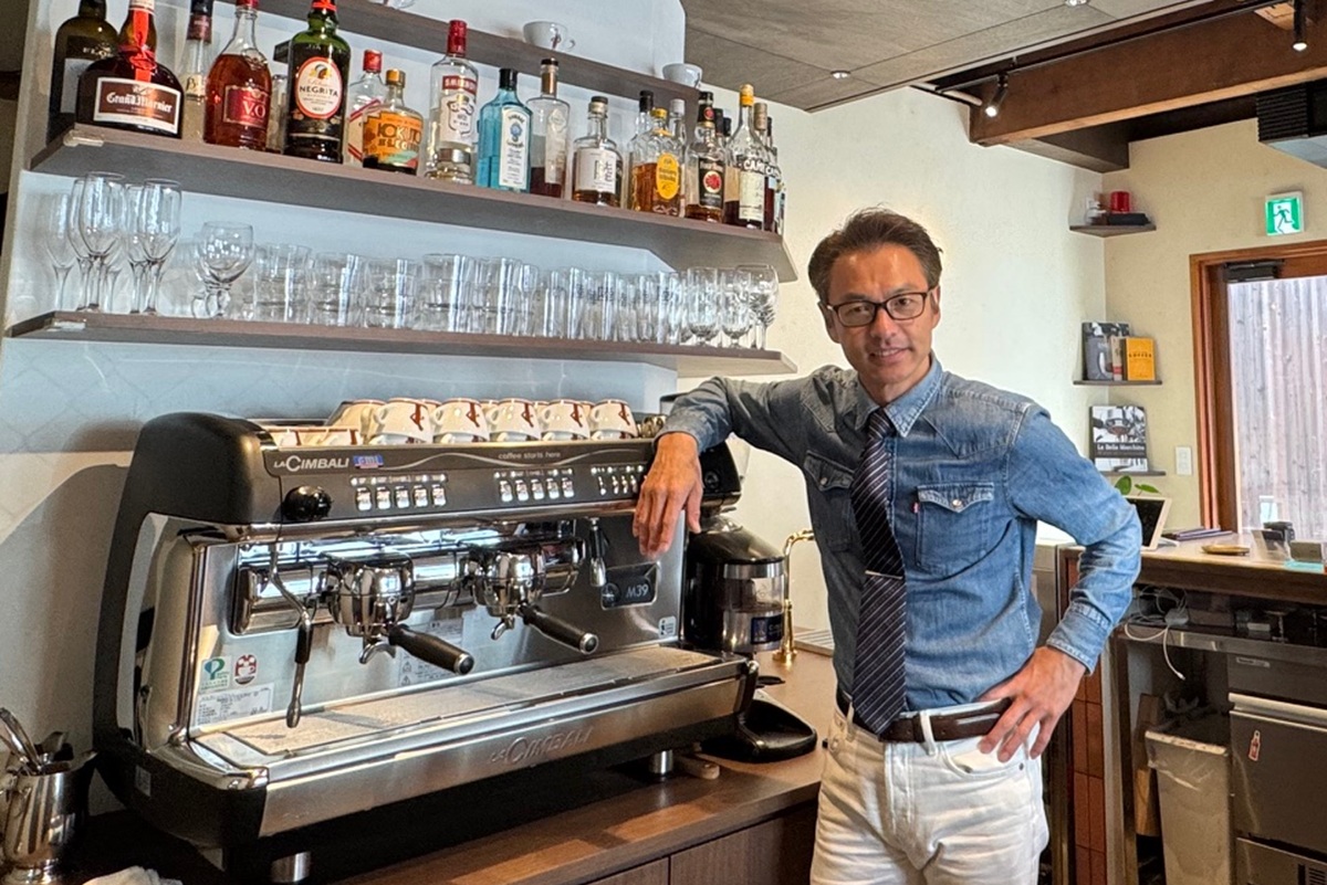 店内に設置されているチンバリ M39の横に立っている岡田章宏様の写真