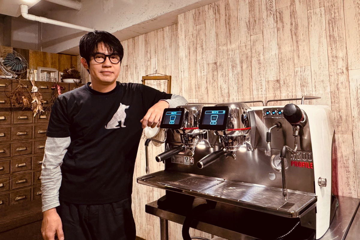 店内に設置されているチンバリ M200の横に立っている小山真様の写真